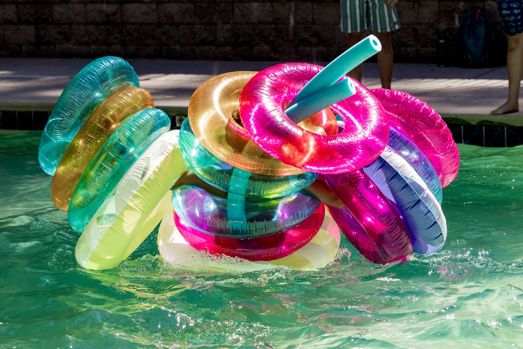 A stack of brightly coloured pool floats drifting on green water