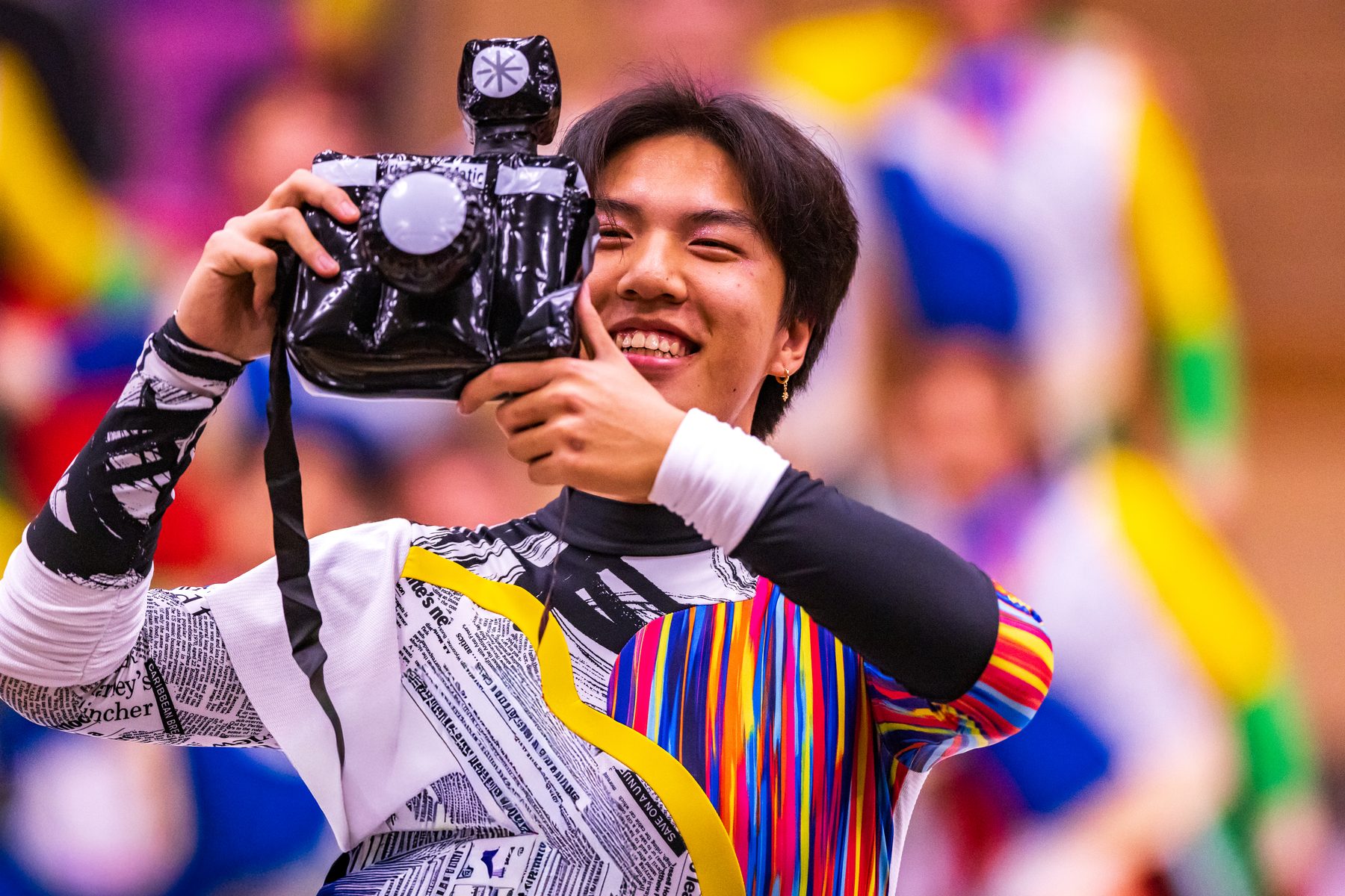 A winter percussion performer in harlequin costume laughing behind a camera