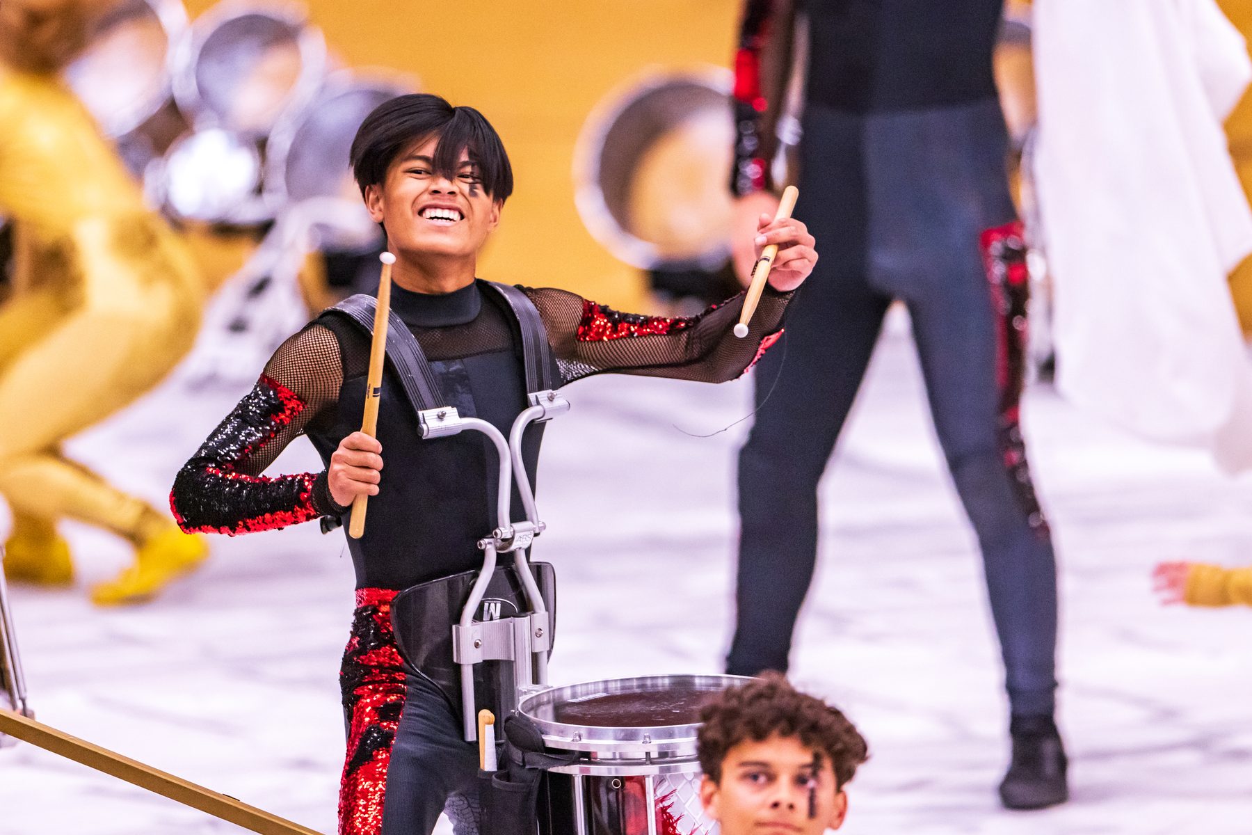A marching snare player mid-strike in black and red
